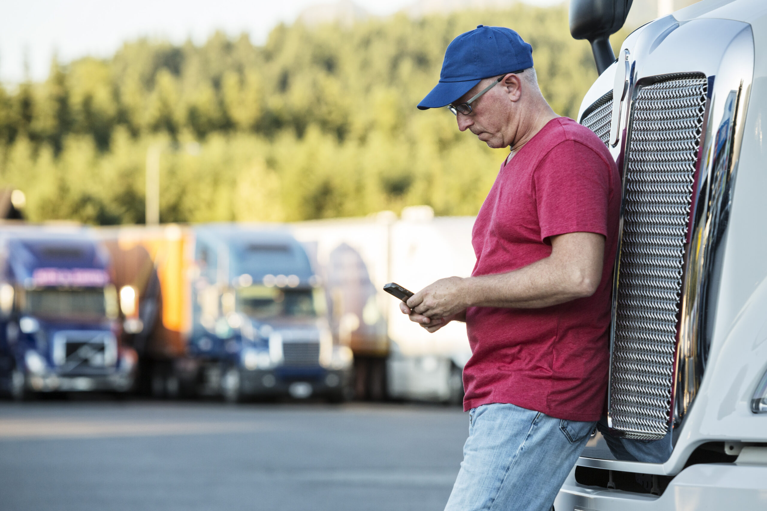 Caucasian man truck driver texting while standing next to the grill of his commercial truck in a struck stop. | fight a CDL roadside ticket