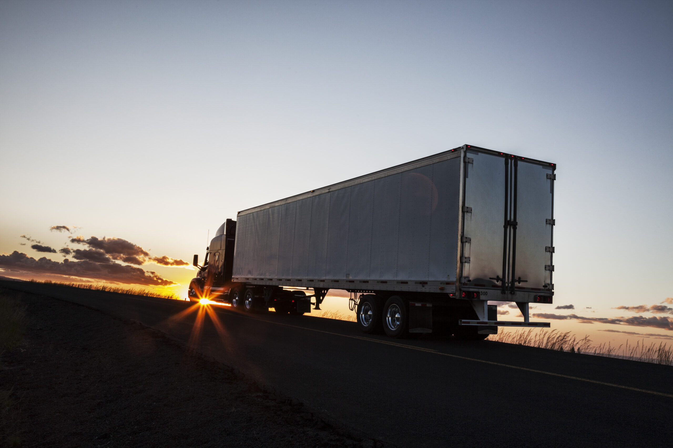 Silhouette of a  commercial truck driving on a highway at sunset.