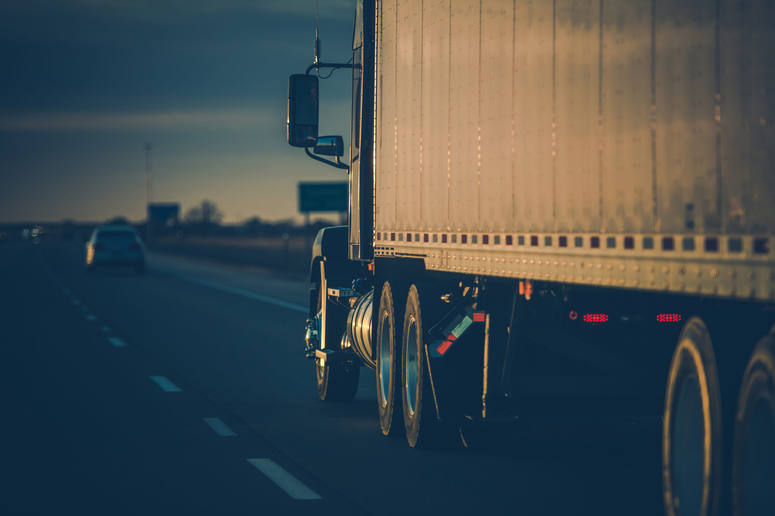 Back View Closeup of American Semi Truck on the Road Driving Forward in Sunset Rays. Transportation Theme.