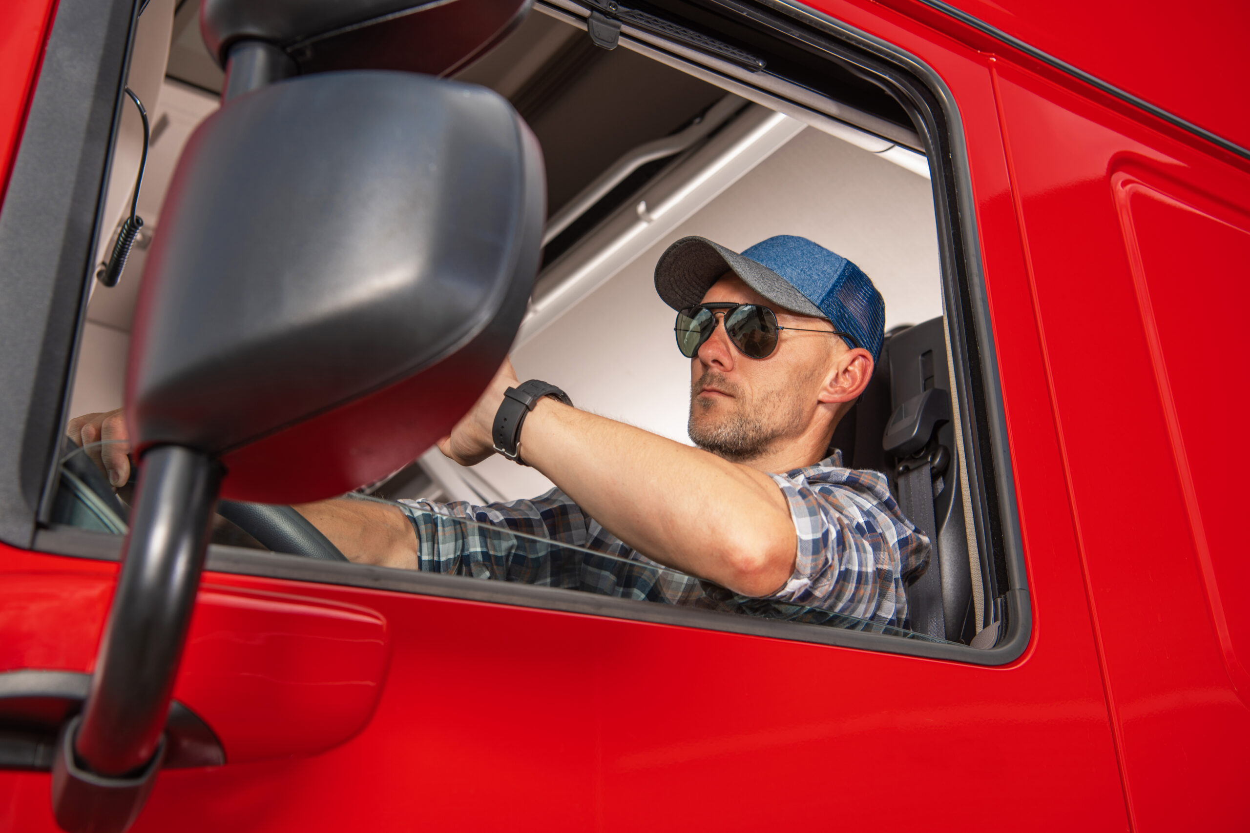 Professional Caucasian Semi Truck Driver in His 40s Behind the Steering Wheel of His Tractor Truck. Heavy Duty Cargo Transportation Theme.